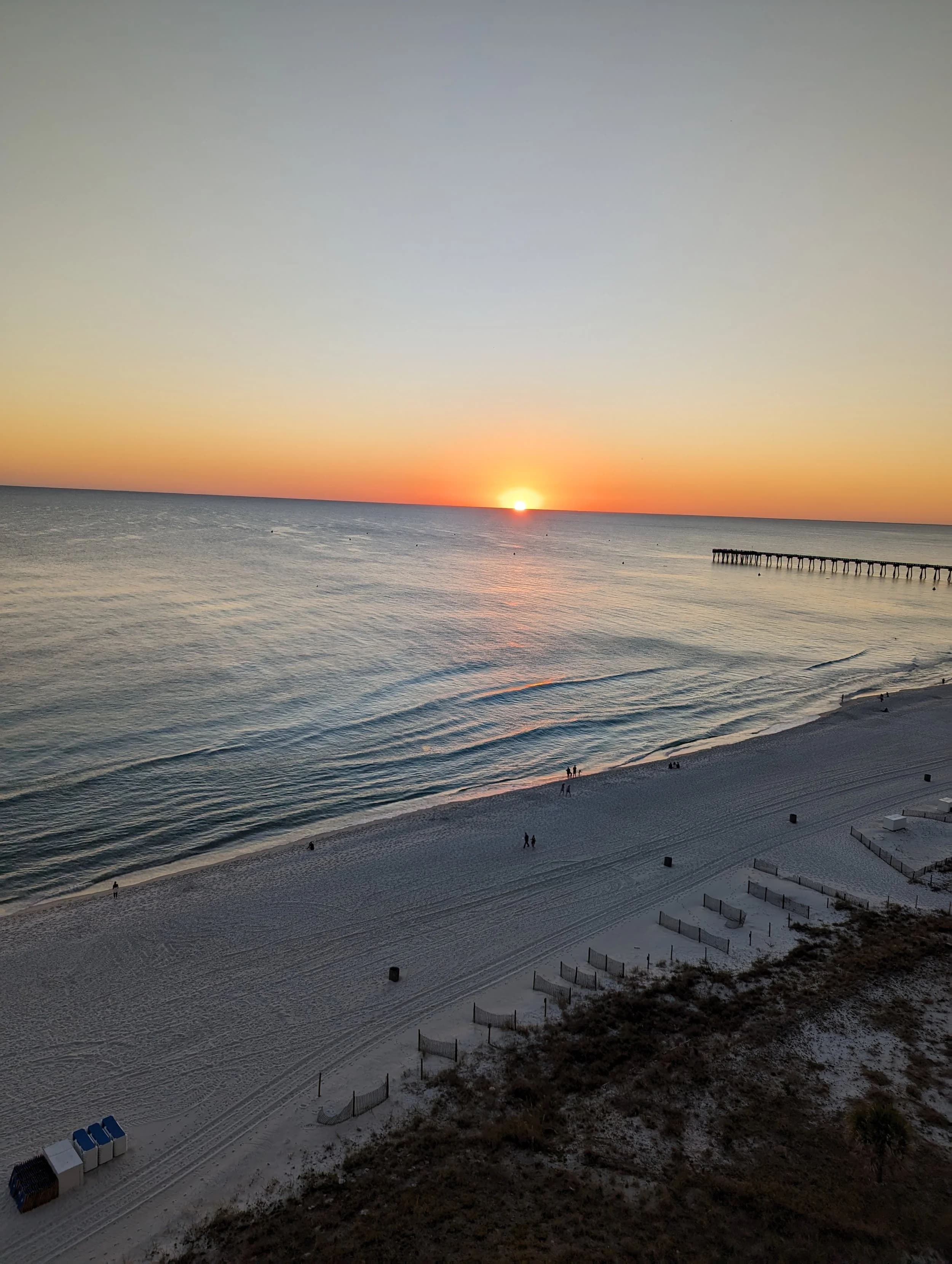 Sunset over a calm ocean with a pier extending into the water